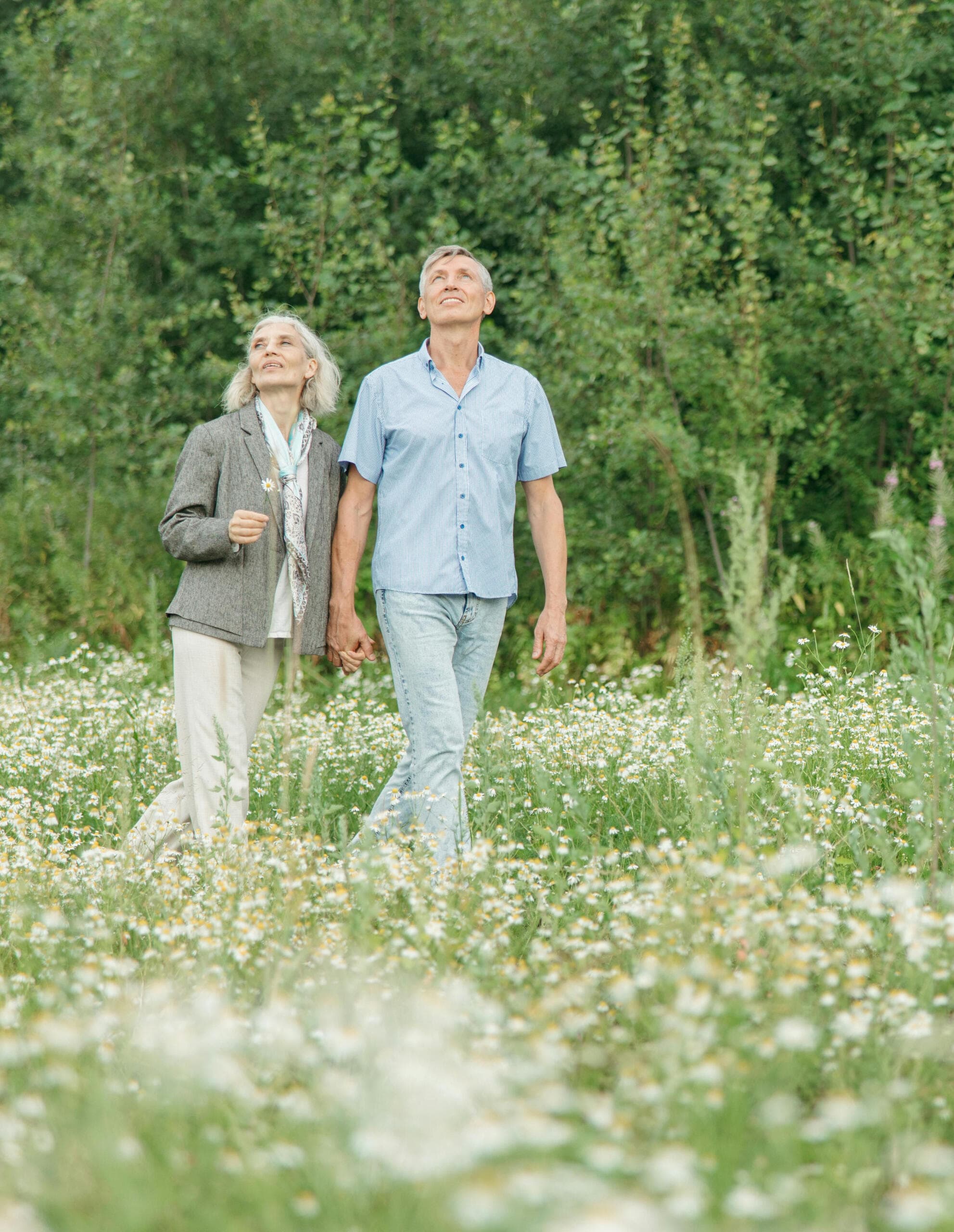An older couple holding hands and walking through a meadow of wildflowers.